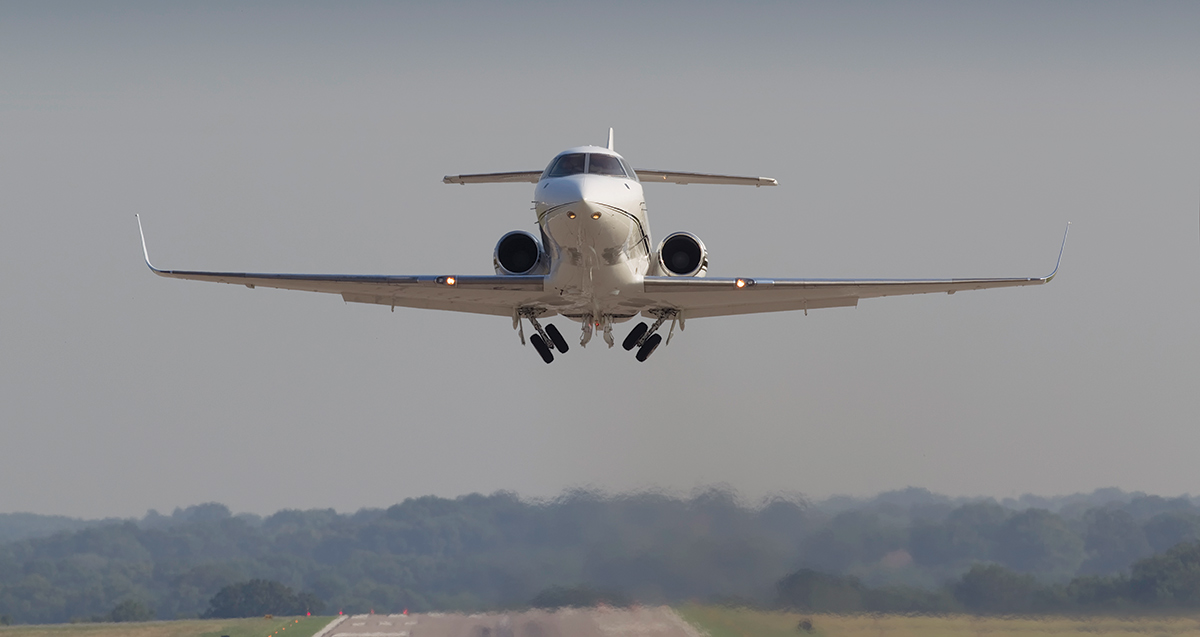 Landscape photograph of a white/silver colored private jet aircraft flying toward the entrance of the airport runway during the day
