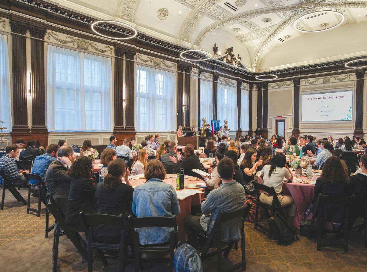 people sitting at tables in room while watching presentation at front of room