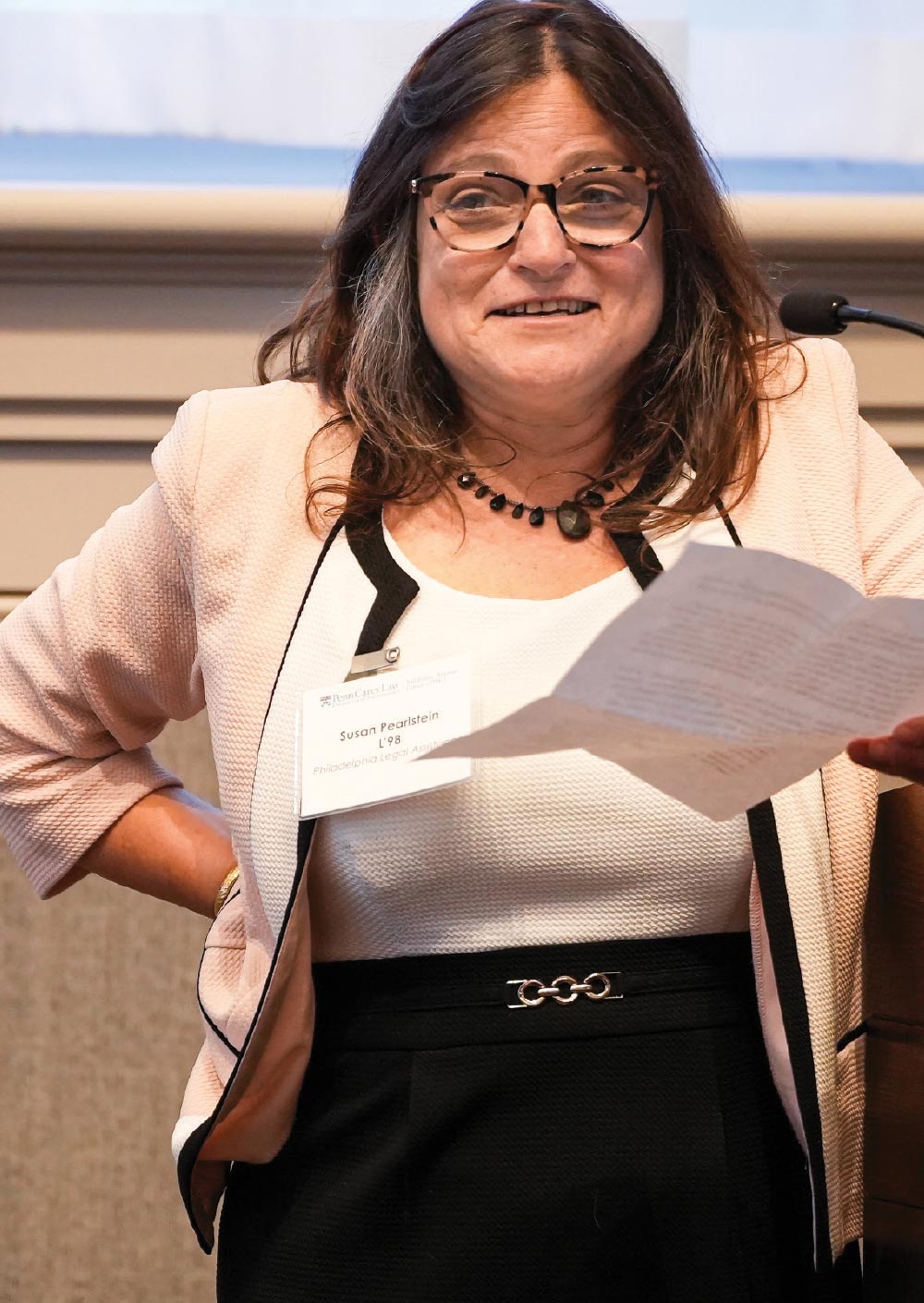 Susan Pearlstein holding a paper while speaking into microphone